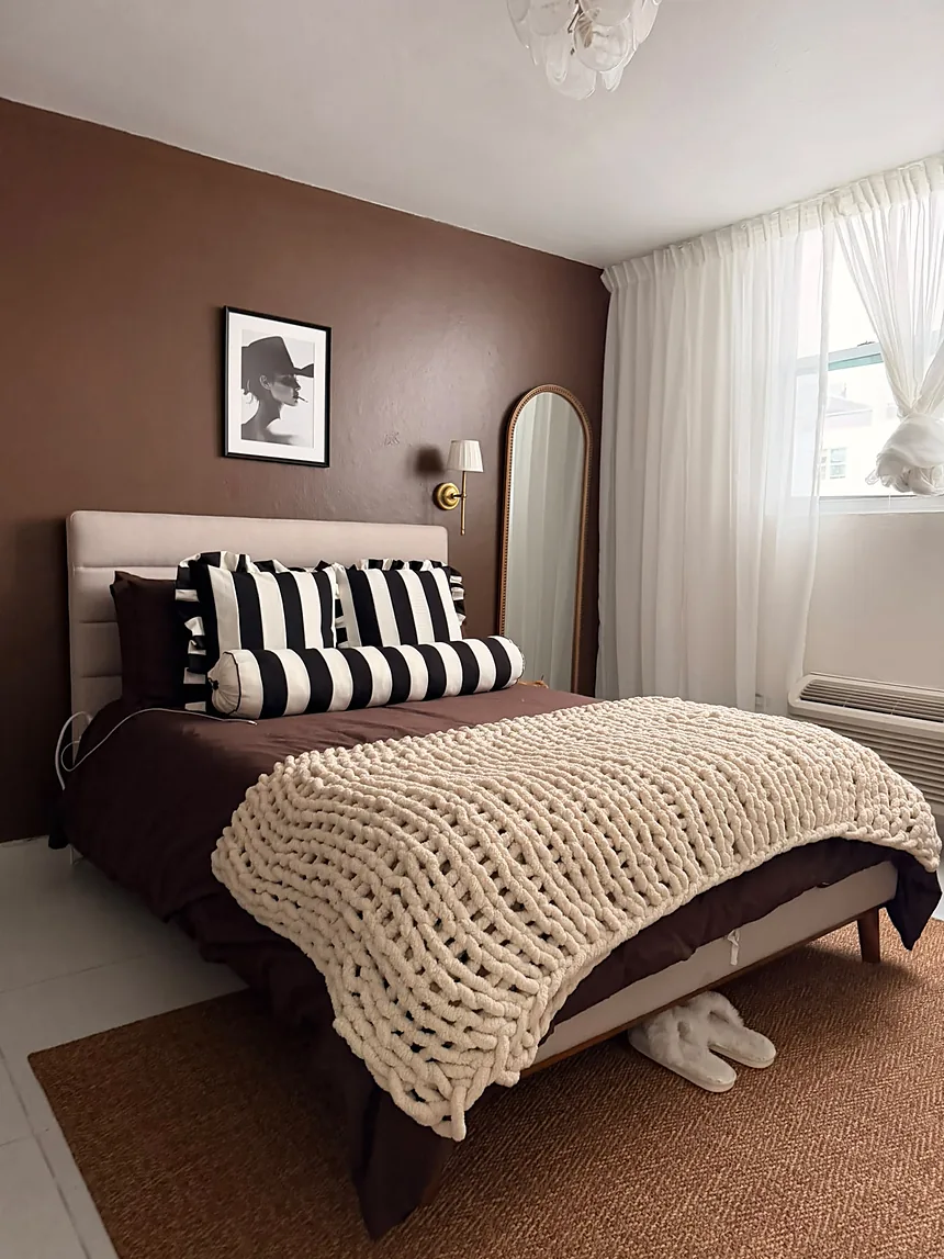 Habitación de un Airbnb con pared marrón, cojines de rayas y manta tejida, lista para recibir huéspedes