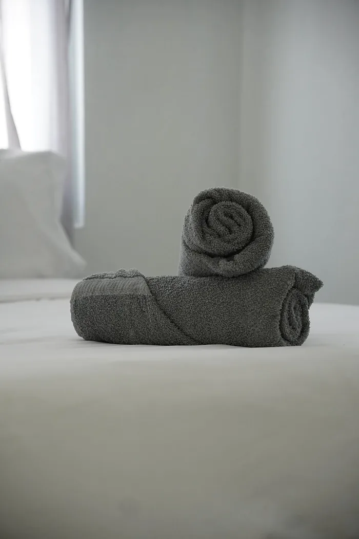 Toallas grises enrolladas y acomodadas sobre la cama tendida de un Airbnb