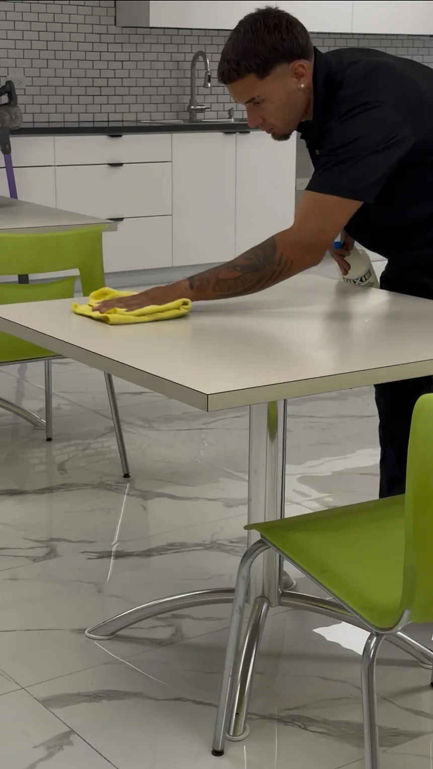 Empleado de Clean Vibes limpiando una mesa del área de comedor de una oficina